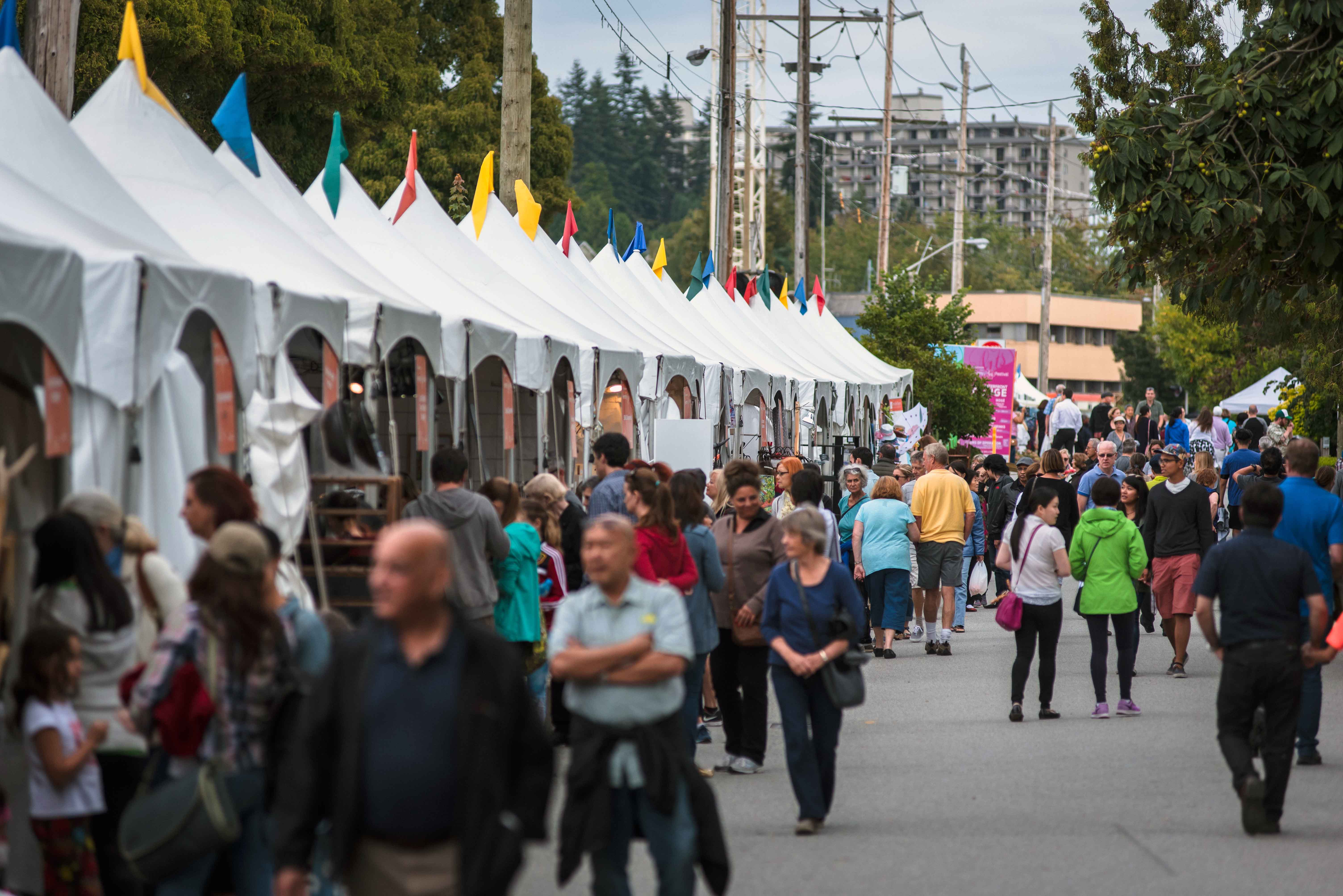 Group of people walking down street with vendor tents on side of road