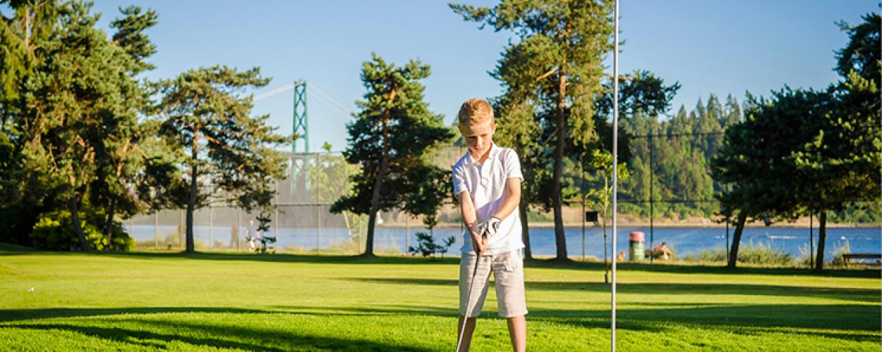 A child putts a golf ball toward the hole marked with a red flag.